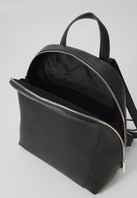 Black leather backpack featuring a smooth texture, silver zipper, and an interior pocket. Minimalist design with top handle and adjustable straps.