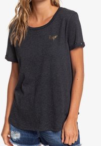 Grå kortærmet t-shirt i blødt materiale, med en afslappet pasform og et diskret guld logo på brystet. Nederkanten er buet med oprullede ærmer.