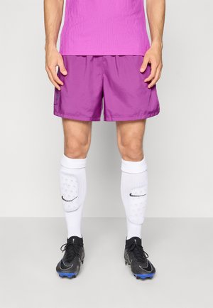 Shorts de sport violets avec une texture lisse, associés à des chaussettes blanches montantes avec un logo Nike noir, et des crampons noirs avec des accents bleus.