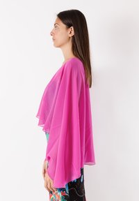 Stola rosa trasparente con ampie maniche fluide drappeggiata su un indumento decorato, che mostra colori vivaci e disegni intricati.