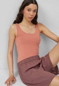 Licht perzik kleurige tanktop met een ronde hals en smalle schouderbandjes, gecombineerd met losse mauve shorts met een elastische tailleband. Soepele stof.