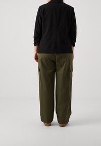 Černé sáčko s límcem a tříčtvrtečními rukávy, kombinované s olivově zelenými širokými kalhotami typu cargo s bočními kapsami.