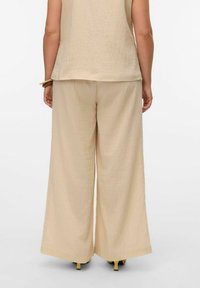 Un pantalon large beige fabriqué à partir d'un tissu texturé avec une coupe décontractée, associé à un haut sans manches assorti, vu de dos.