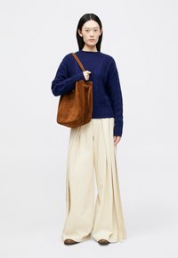 Μπλε πουλόβερ με πλέγμα καλωδίου και μακριά μανίκια, σε συνδυασμό με κρεμ παντελόνια με φαρδιά πόδια και καφέ σουέτ τσάντα ώμου. Καφέ παπούτσια ολοκληρώνουν το σύνολο.