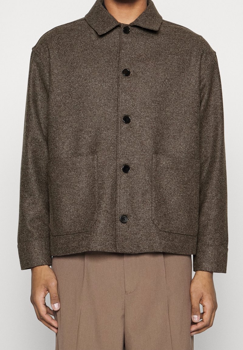 Veste en laine marron avec un col, boutons sur le devant et deux grandes poches, présentant une finition texturée et une silhouette ample.