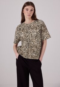 Tričko s krátkým rukávem s leopardím potiskem v hnědé a černé barvě, s kulatým výstřihem a volným střihem. S kombinací černých kalhot.