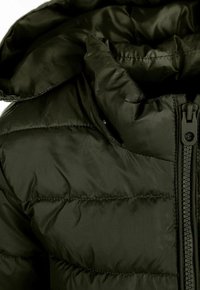 Veste matelassée vert foncé avec un design capitonné. Elle possède un col haut, une fermeture zippée intégrale et une texture lisse et brillante.