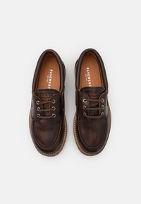 Chaussures en cuir marron à bout rond, design à lacets, semelle contrastante marron clair ; surface texturée et détails de couture en relief.