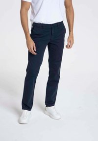 Chinos bleu marine à coupe ajustée, dotés de poches latérales, d'une taille à bouton et d'un tissu en coton lisse. Associés à des baskets blanches et un t-shirt blanc.