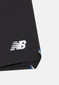 Črne športne hlače z belim logotipom New Balance ter modrimi in zlatimi črtami na robu.