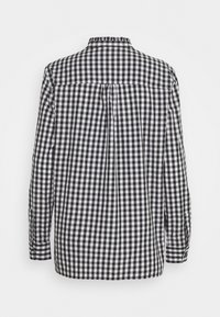Camicia a maniche lunghe a scacchi in bianco e nero, con colletto alto, polsini con bottone e dettaglio plissettato sul retro, realizzata in un tessuto leggero.
