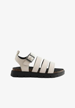 Sandalias gris claro que cuentan con tres correas anchas, un hebilla, plantilla con textura de corcho y suela de goma negra con surcos para mayor agarre.