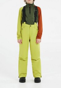 Pantaloni da neve impermeabili di un brillante giallo, con spallacci neri regolabili, tasche laterali e una vestibilità comoda. Abbinati a una maglietta a maniche lunghe verde e marrone.