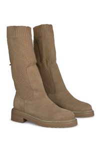 Botas beige hasta la rodilla con un upper de punto texturizado y una parte inferior de ante suave, que presentan una suela plana y un borde decorativo plateado alrededor de la base.