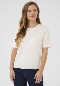 Kurzärmliges Oberteil in Cremefarbe aus weichem Stoff, mit rundem Ausschnitt und lockerem Schnitt, kombiniert mit dunkelblauen Jeans.