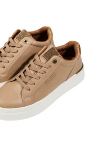 Sneakers in pelle beige con punta rotonda, suola bianca piatta, accentuazione testurizzata sul tallone e dettagli decorativi sulla linguetta. Lacci passanti attraverso i fori.