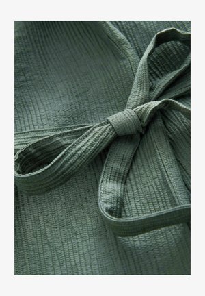 Tessuto verde oliva con texture e sottili linee verticali, caratterizzato da un dettaglio con nastro legato. Il materiale appare morbido e leggero.
