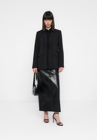 Blazer nero su misura con rever a punta, due tasche frontali, abbinato a una lunga gonna in pelle nera e tacchi neri con cinturini. Accessorio borsa nera.