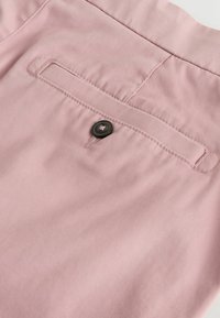 Poche arrière d'un pantalon rose clair avec un bouton noir et des détails de couture soignés sur un tissu lisse.