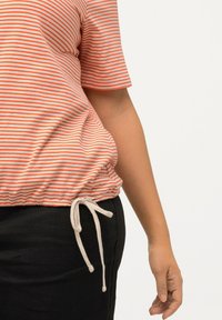 Top a rayas en rojo y blanco de algodón, con dobladillo fruncido y detalle de cordón. Mangas cortas y corte relajado, combinado con pantalones oscuros.
