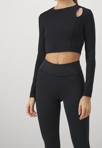 Black long-sleeve crop top with a round neckline and a side cutout, paired with high-waisted black leggings featuring a smooth texture.