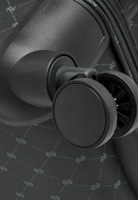 Assemblaggio delle ruote di una valigia nera con un'esterno testurizzato e un design circolare delle ruote. Caratterizzato da un robusto montaggio e un intricato motivo sulla superficie.