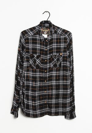Black, white, and orange plaid long-sleeve shirt with buttons and two chest pockets hanging on a black hanger against a white background.