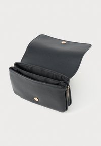 Svart läderclutch med öppet lock, som avslöjar två huvudfack och ett guldfärgade knäppning på en ljus bakgrund.