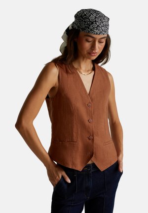 Rust brown linen vest with a V-neck, five buttons, and side pockets; worn over dark denim pants, accompanied by a patterned headscarf.