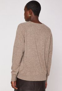 Maglione a maglia color sabbia con orlo e polsini a coste, caratterizzato da una vestibilità rilassata e una consistenza sottile. Indossato con una gonna in pelle marrone.