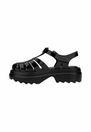 Black rubber sandals with a closed toe design, featuring horizontal cutouts and a thick, textured sole for grip. Adjustable strap included.