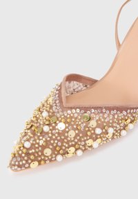 Béžová špičatá topánka zdobená zlatými flitrami, korálkami a bielymi perlami na vrchnej časti z jemnej látky s remienkom na členku.