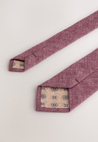 Burgundy woven tie with a textured finish. Inner lining features a floral pattern on a beige background. Angled tips with stitched accents.