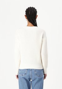 Biały sweter z dzianiny o prążkowanej fakturze, okrągłym dekolcie i obniżonych ramionach, zestawiony z jasnoniebieskimi dżinsami. Prosty i casualowy design.