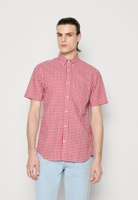 Chemise à manches courtes à carreaux rouges et blancs avec un col boutonné et un logo brodé sur la poitrine. Fabriquée en tissu léger.