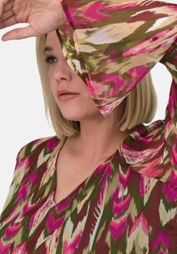Blusa multicolore con scollatura a V, caratterizzata da un motivo floreale nei toni del rosa, verde e crema. Le maniche a campana aggiungono texture.
