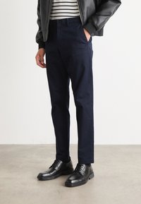 Marinblå byxor med skräddarsydd passform, tillverkade av lättviktig tyg. Kombinerat med svarta snörskor och en randig skjorta under en bomberjacka.