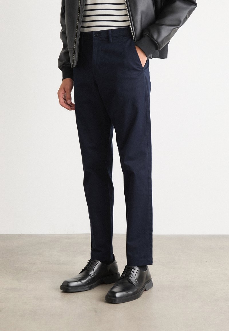 Marinblå byxor med skräddarsydd passform, tillverkade av lättviktig tyg. Kombinerat med svarta snörskor och en randig skjorta under en bomberjacka.