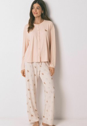 Lyserød pyjamasbluse med rund hals og knaplukning, kombineret med cremefarvede bukser med stribet mønster og små peberkagedesigns.