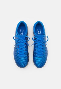 Zapatos de fútbol azules con parte superior sintética texturizada, cordones a juego y un cuello acolchado. Presenta un logo de Nike en blanco y una plantilla acolchada.