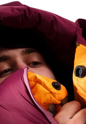 Giacca a vento bordeaux con interno arancione. Include una zip e dettagli in metallo nero, con un tessuto esterno testurizzato.