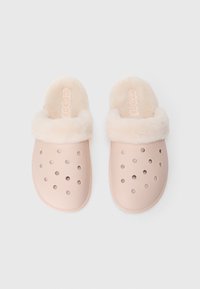 Une paire de Crocs rose clair avec doublure en fourrure et trous de ventilation, conçues pour le confort et la chaleur à l'intérieur.