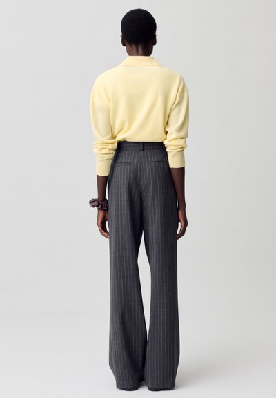 Suéter de punto amarillo claro con cuello, combinado con pantalones de tiro alto de rayas grises. Tela texturizada visible en ambas prendas.