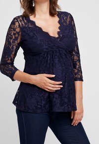 Marinblå spets graviditetstopp med skulpterad halsringning och trekvartslång ärm. Har en lös passform med blomster mönster och texturerat tyg.