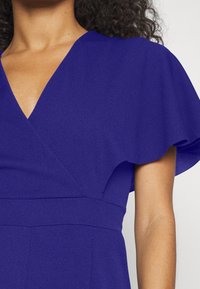 Vestido de cuello en V en tela sólida de azul profundo, con mangas de volante y una cintura ajustada. Textura suave con una silueta elegante.