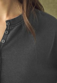Chemise henley gris foncé avec un col côtelé, trois petits boutons gris et un tissu doux et texturé.