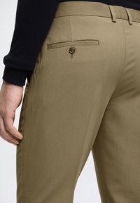 Khaki broek van een gladde, gestructureerde stof, met een achterzak met knoopsluiting en details op de zijnaden.