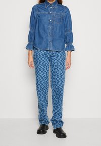 Jeansskjorta med knappframsidan och puffärmar, parat med mönstrade blå byxor med geometriska mönster och svarta skor.