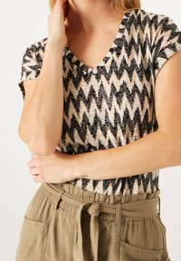 V-neck top in a black, cream, and brown zigzag pattern; paired with khaki high-waisted pants featuring a tied waist and side pockets.