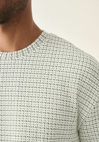 Light gray knitted sweater featuring a textured pattern with black accents, crew neckline, and short sleeves.